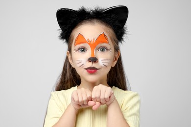 Photo of Cute girl with painted face and ears as cat on grey background