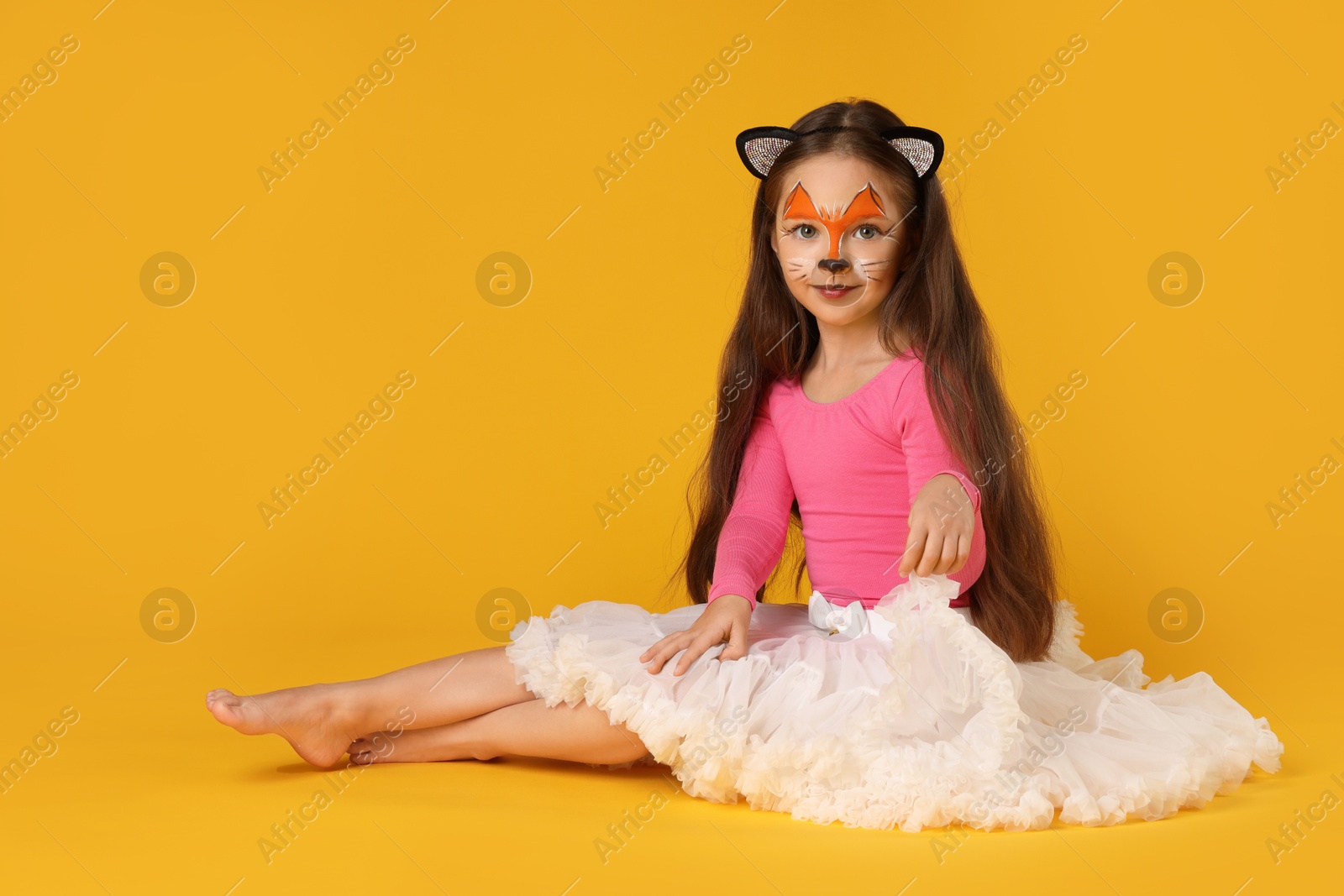 Photo of Cute girl with painted face and ears as cat on orange background