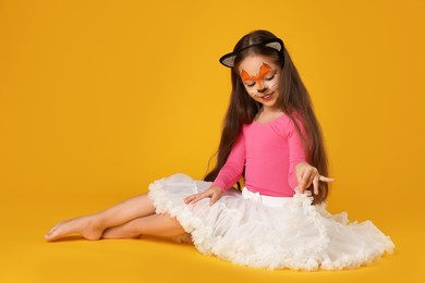 Photo of Cute girl with painted face and ears as cat on orange background