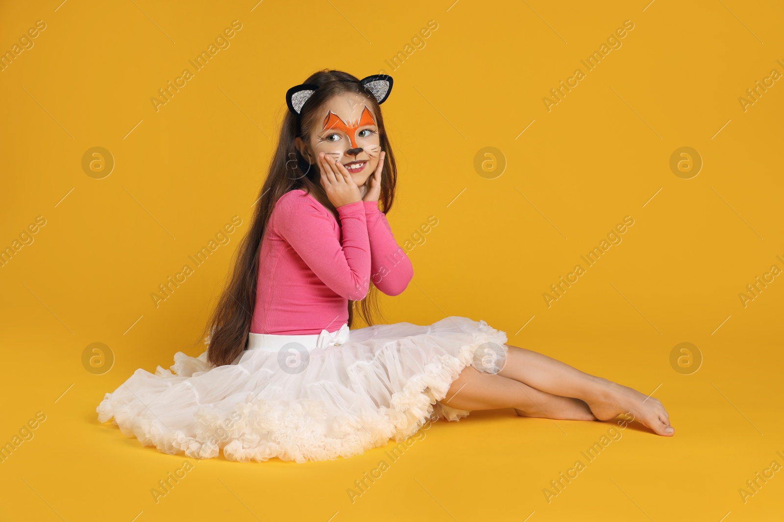 Photo of Cute girl with painted face and ears as cat on orange background