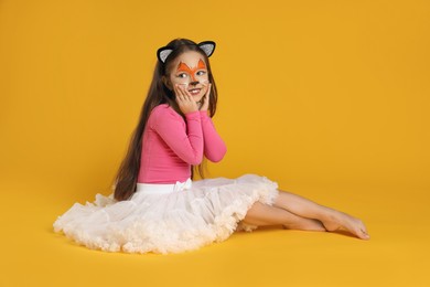 Photo of Cute girl with painted face and ears as cat on orange background