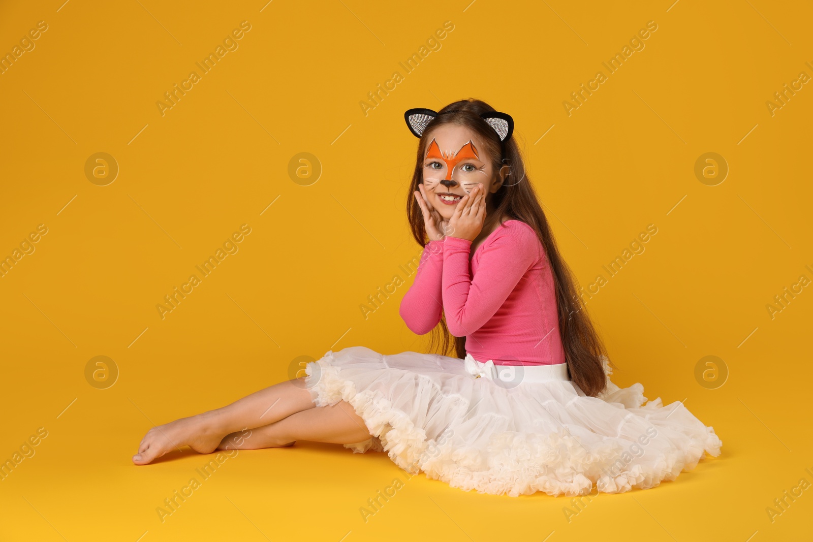 Photo of Cute girl with painted face and ears as cat on orange background