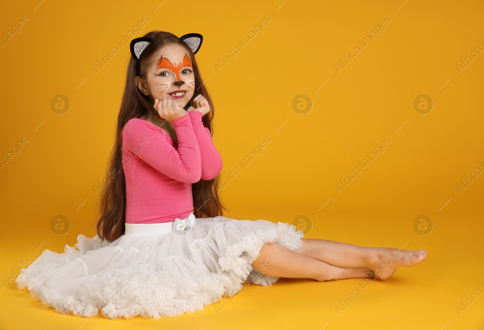 Photo of Cute girl with painted face and ears as cat on orange background, space for text