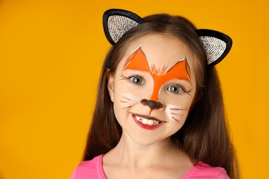 Photo of Cute girl with painted face and ears as cat on orange background