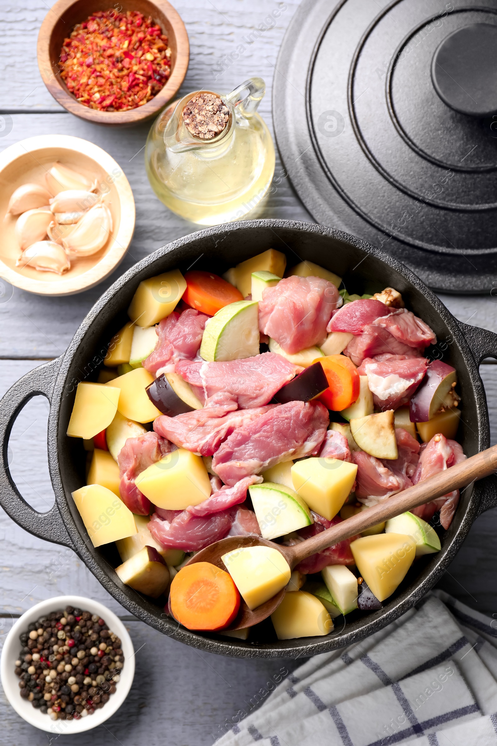 Photo of Cooking stew. Uncooked meat and vegetables in pot on light grey wooden table, flat lay