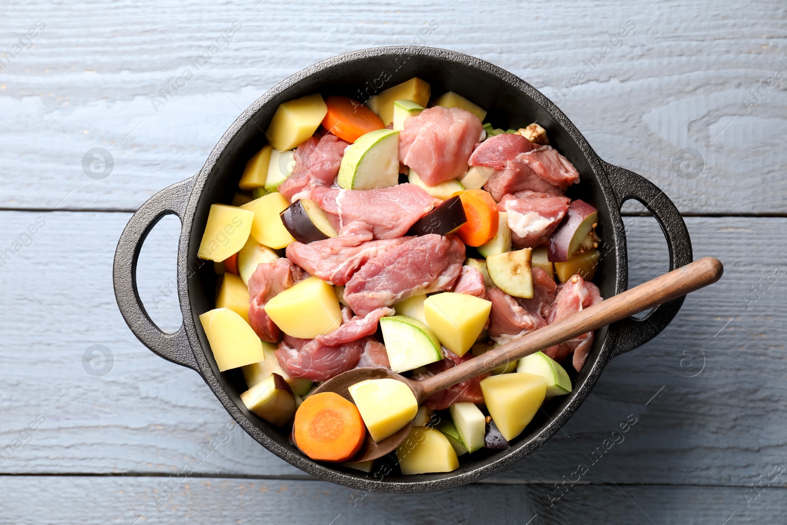 Photo of Cooking stew. Uncooked meat and vegetables in pot on light grey table, top view