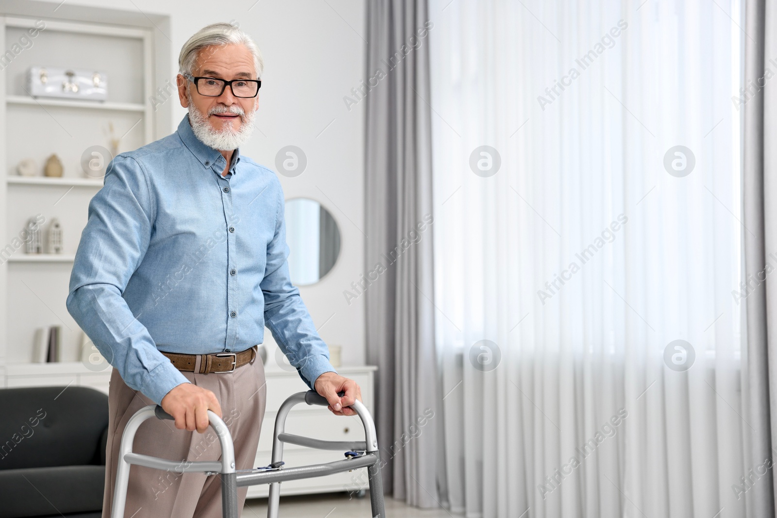 Photo of Senior man using walking frame at home. Space for text