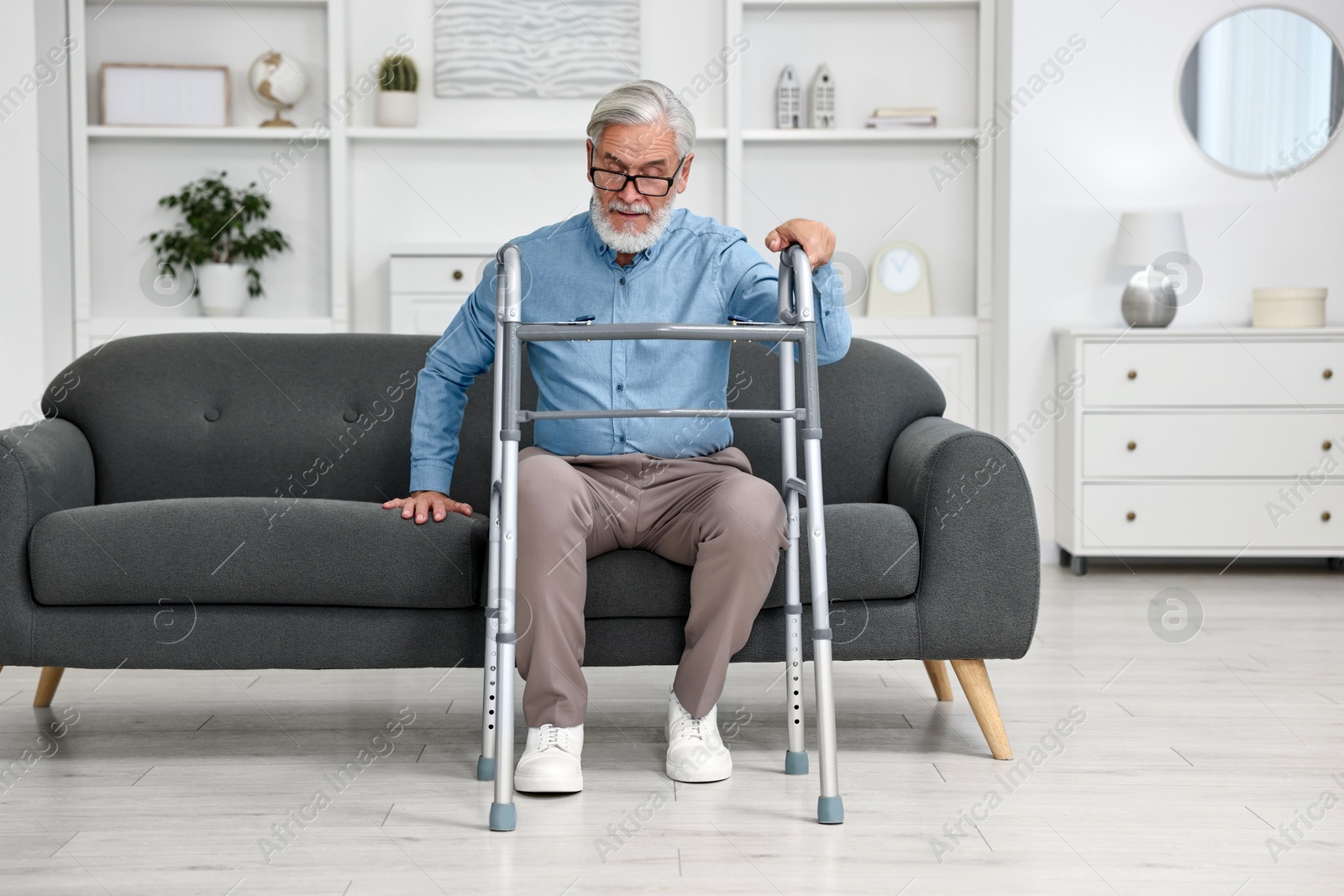 Photo of Senior man with walking frame on sofa at home