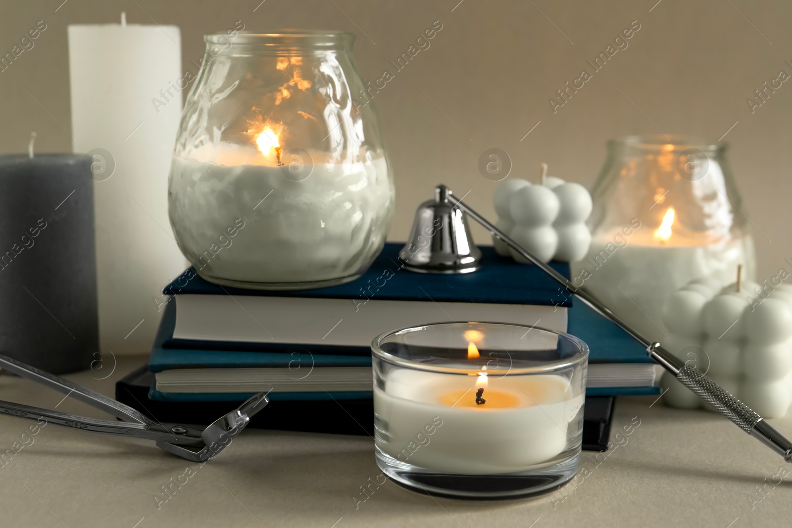 Photo of Beautiful burning candles, books, candle snuffer and wick trimmer on gray table, closeup