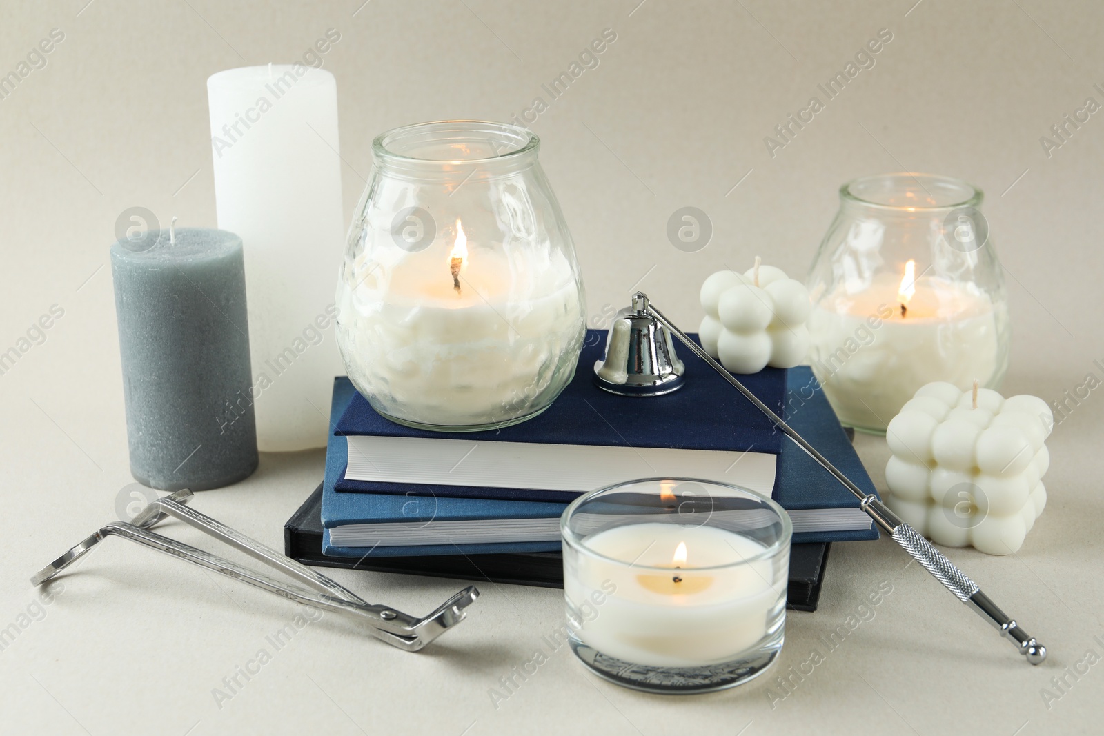 Photo of Beautiful burning candles, books, candle snuffer and wick trimmer on light background