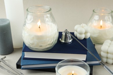 Photo of Beautiful burning candles, books, candle snuffer and wick trimmer on light table, closeup