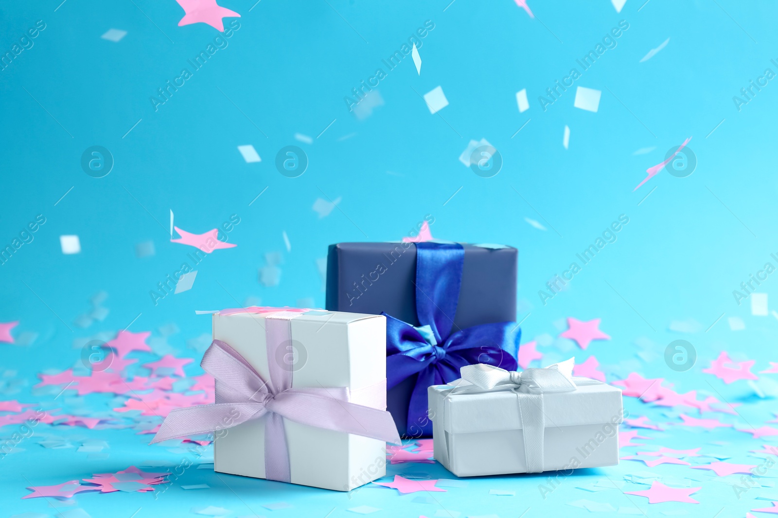 Photo of Beautiful confetti falling on gift boxes against light blue background