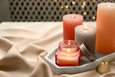 Photo of Beautiful burning candles on fabric against blurred lights. Space for text