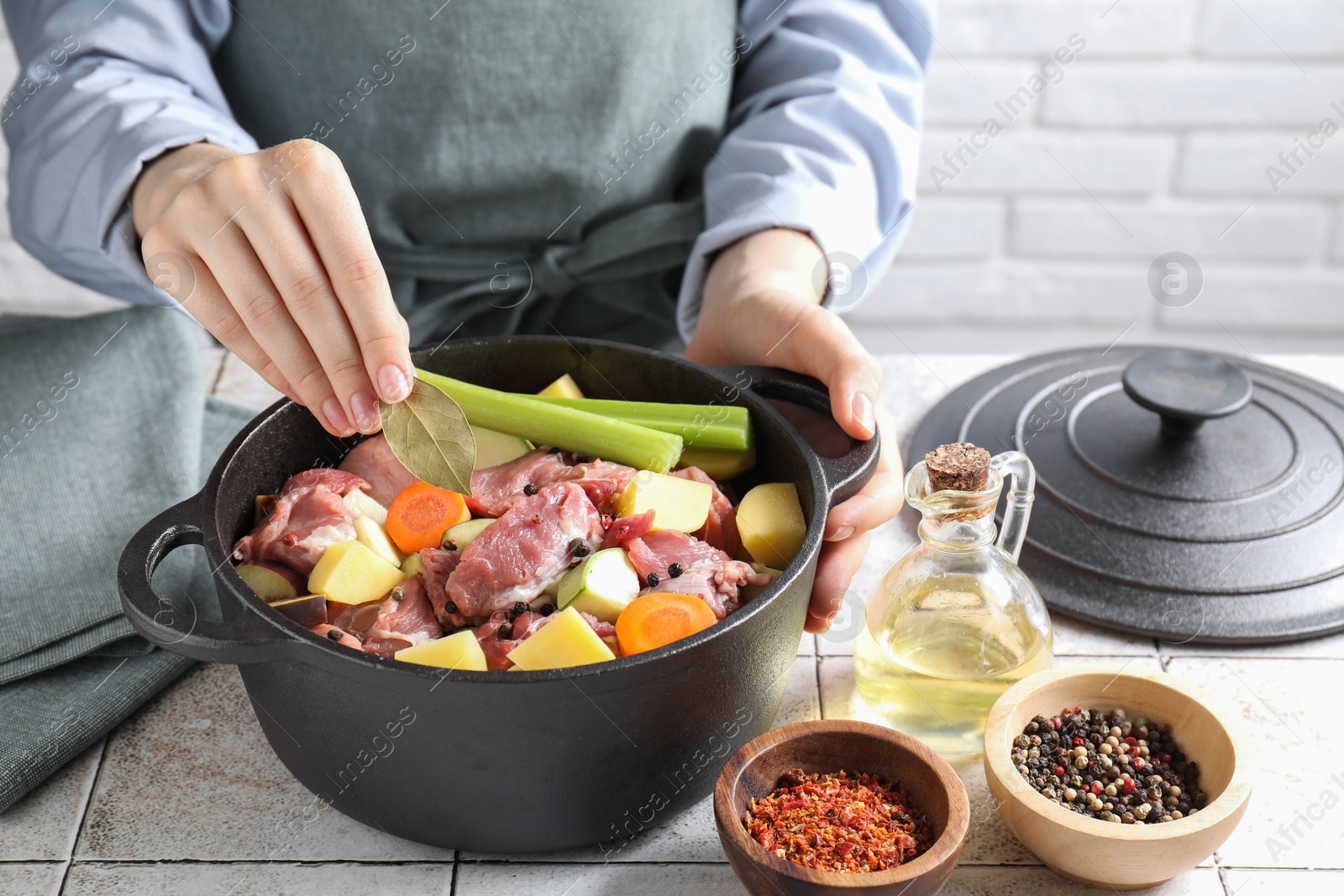 Photo of Woman preparing stew with vegetables and meat at white tiled table, closeup