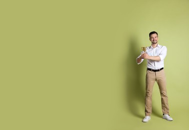 Photo of Happy winner with golden trophy cup on pale olive background