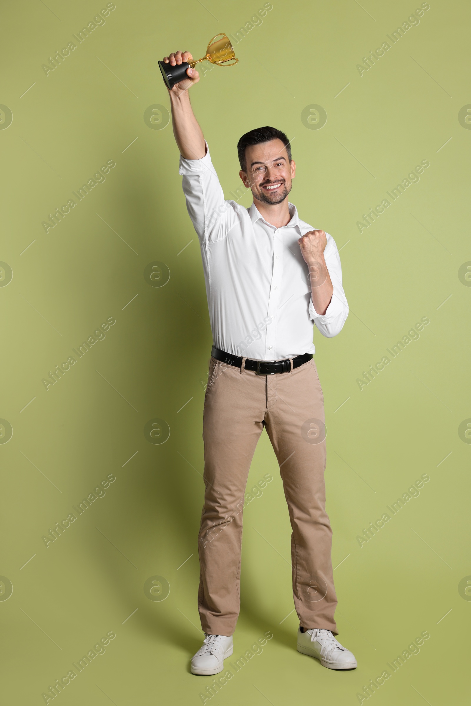 Photo of Happy winner with golden trophy cup on pale olive background