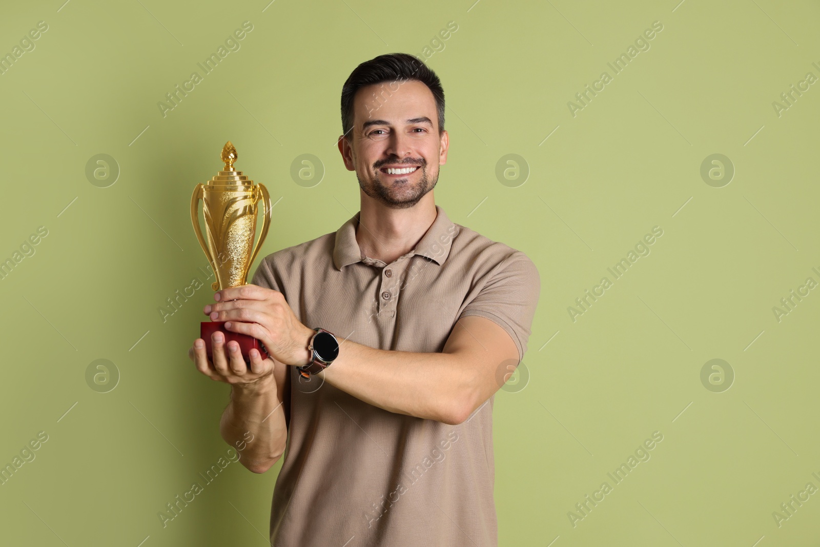 Photo of Happy winner with golden trophy cup on pale olive background