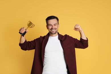 Photo of Happy winner with golden trophy cup on yellow background