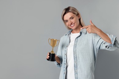 Photo of Happy winner with golden trophy cup on gray background, space for text