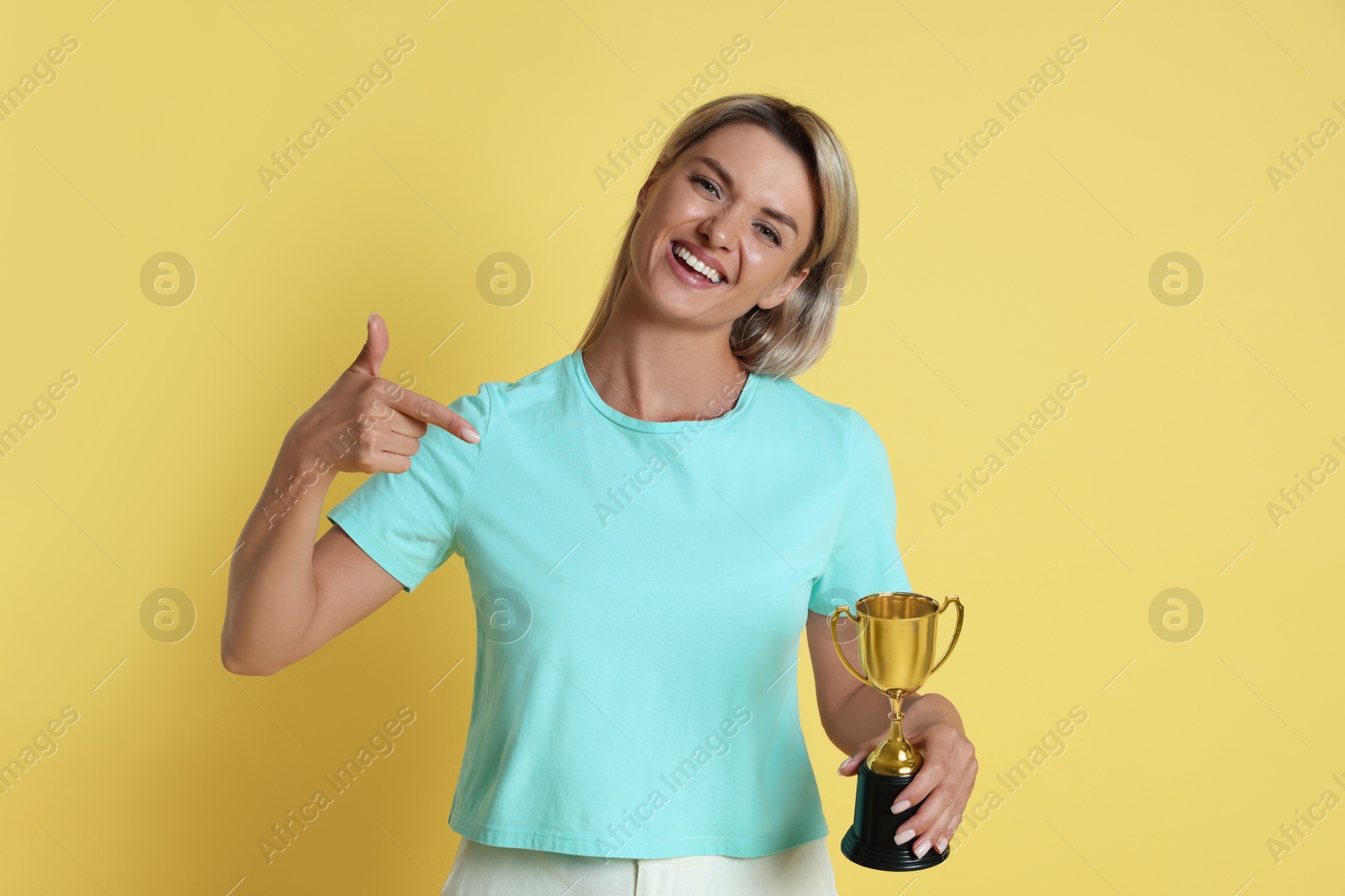 Photo of Happy winner with golden trophy cup on yellow background