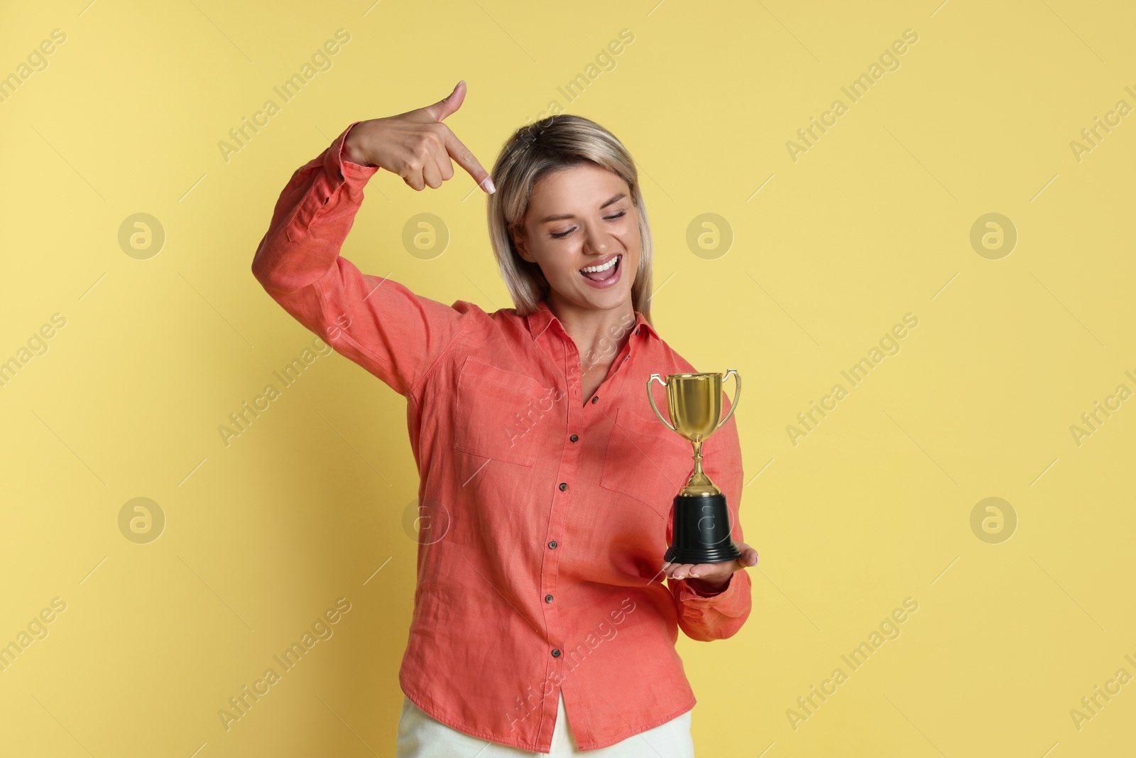 Photo of Happy winner with golden trophy cup on yellow background