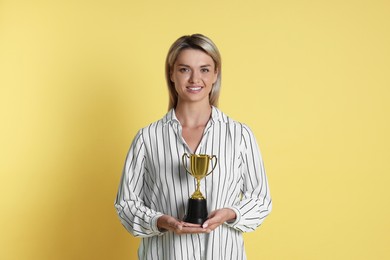 Photo of Happy winner with golden trophy cup on yellow background