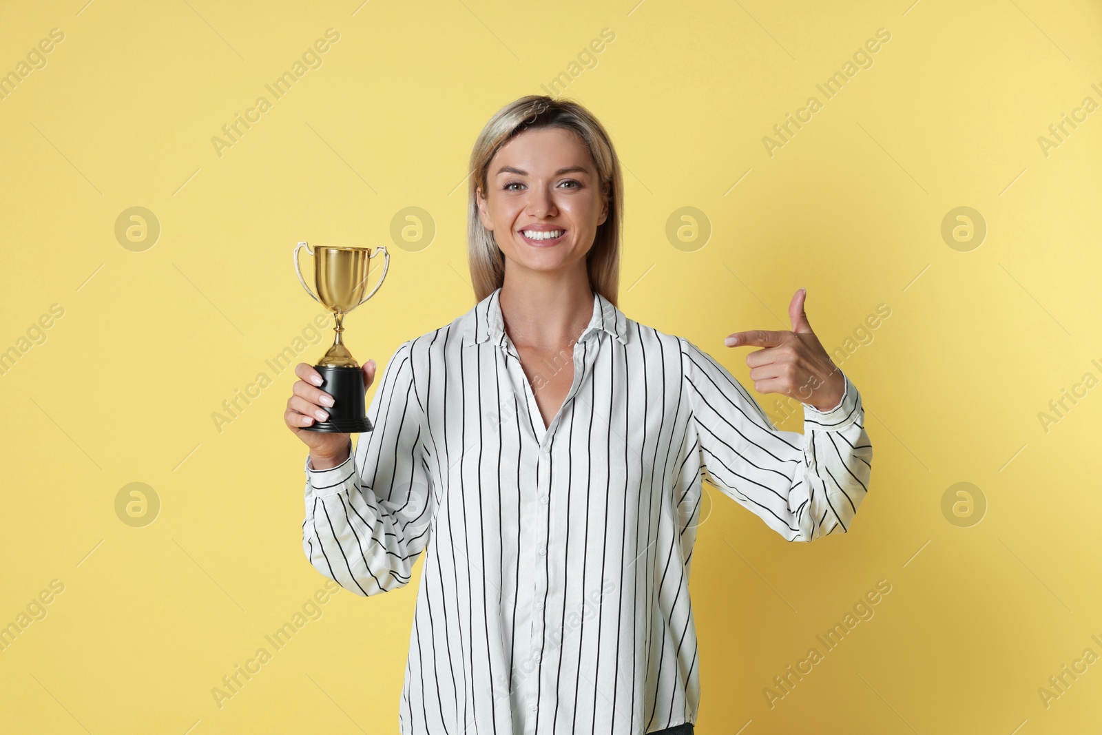 Photo of Happy winner with golden trophy cup on yellow background