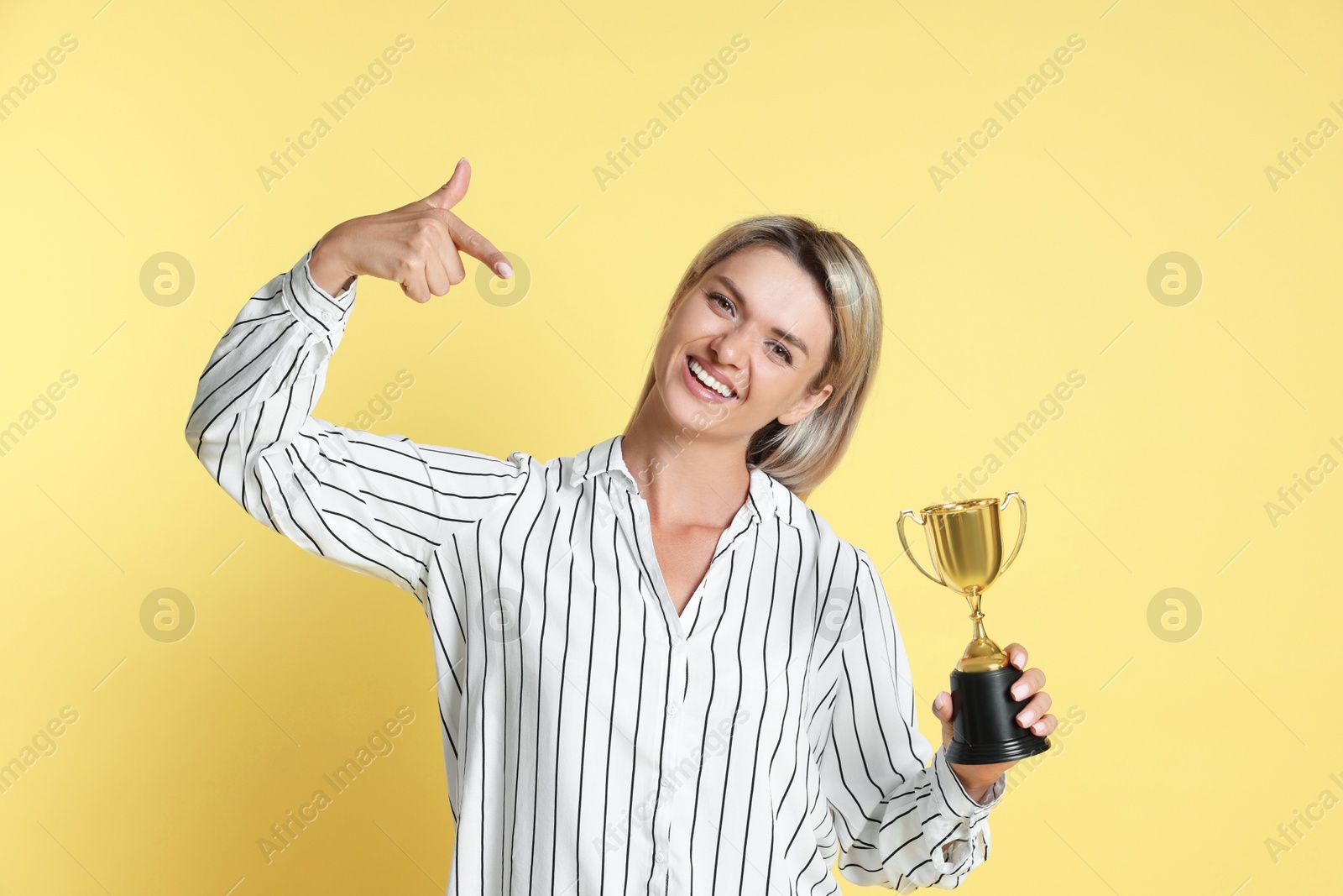 Photo of Happy winner with golden trophy cup on yellow background