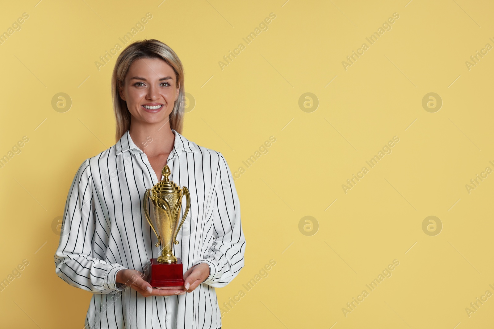 Photo of Happy winner with golden trophy cup on yellow background, space for text