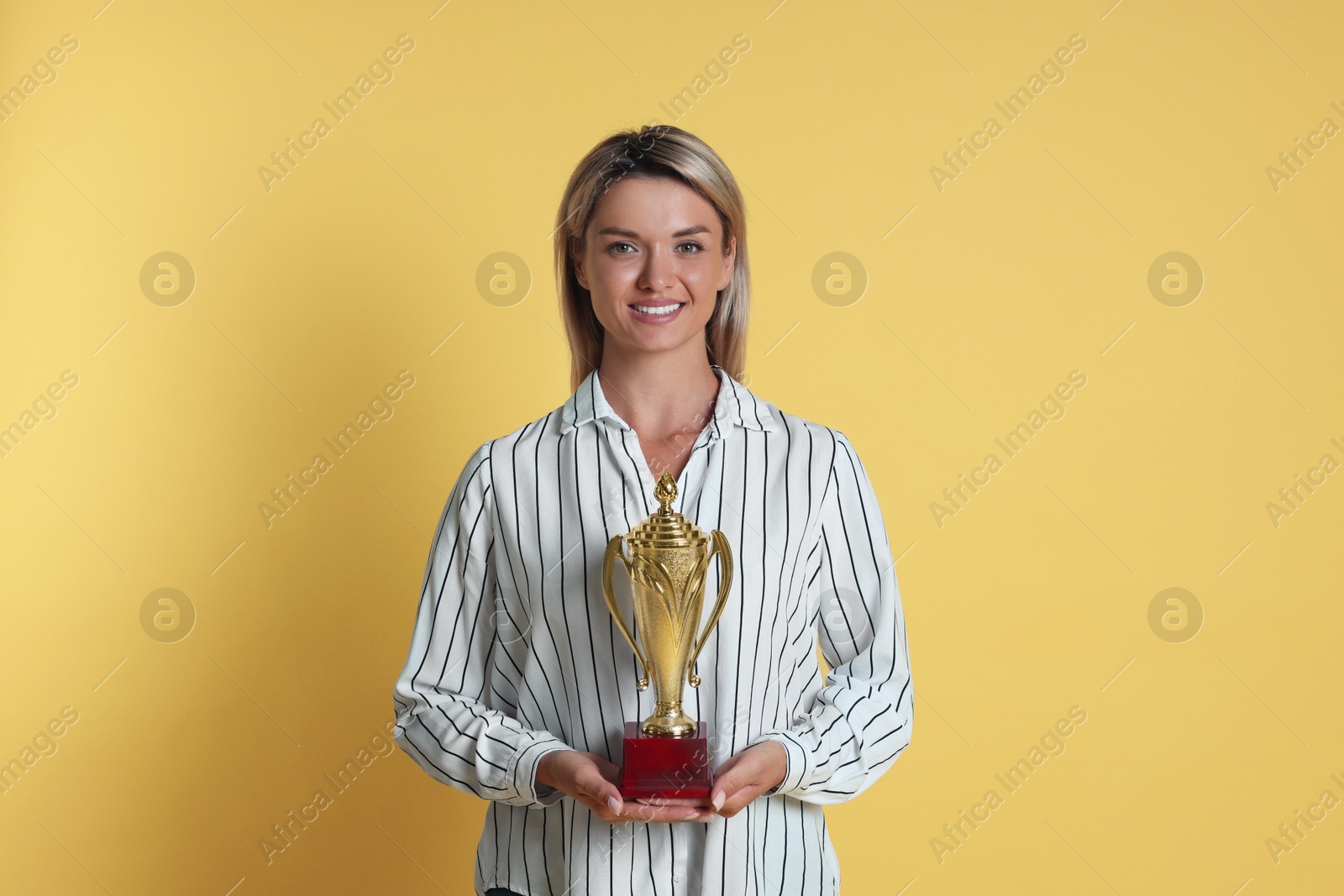 Photo of Happy winner with golden trophy cup on yellow background