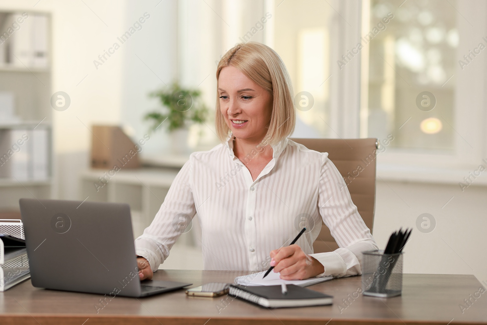 Photo of Smiling middle aged woman working with laptop at table in office