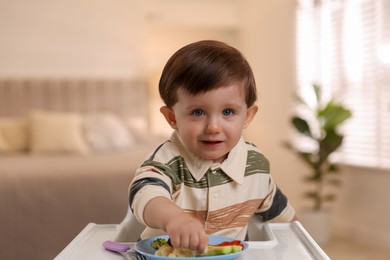 Photo of Cute little baby eating healthy food in high chair at home