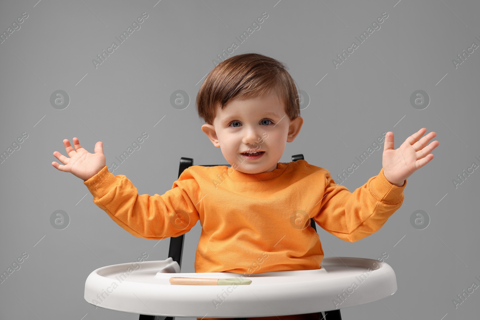 Photo of Cute little kid with spoon sitting in high chair on light grey background