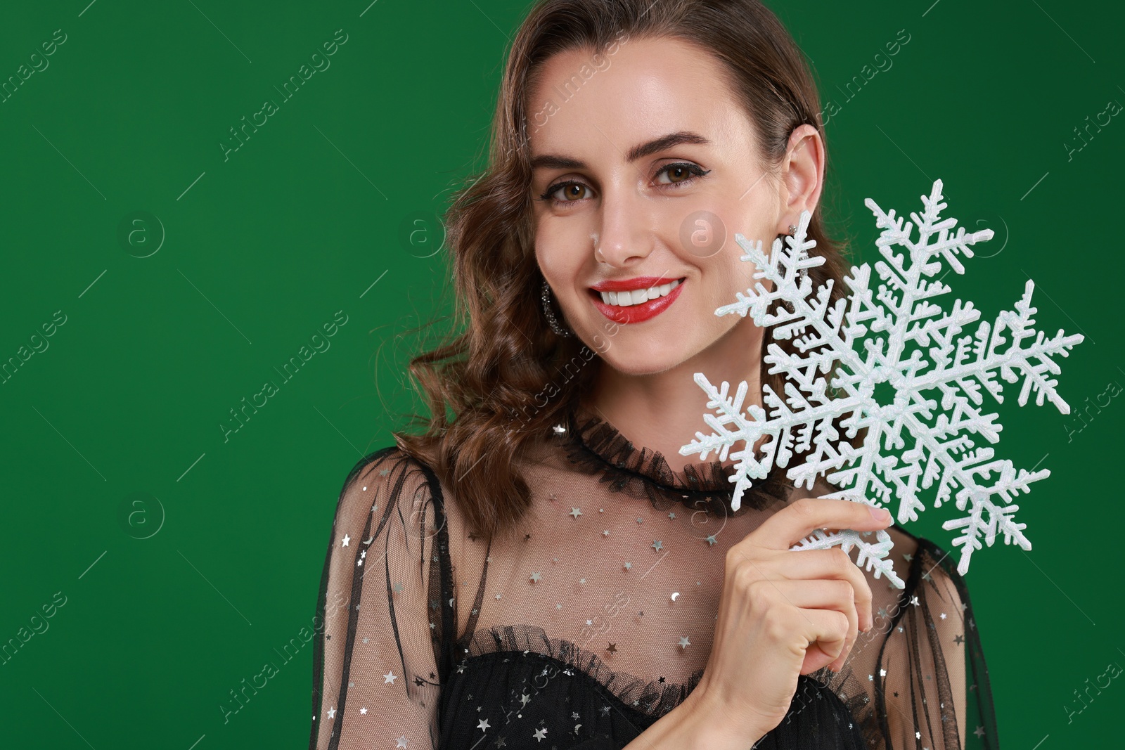 Photo of Smiling woman with perfect makeup holding decorative snowflake on green background, space for text. Christmas celebration