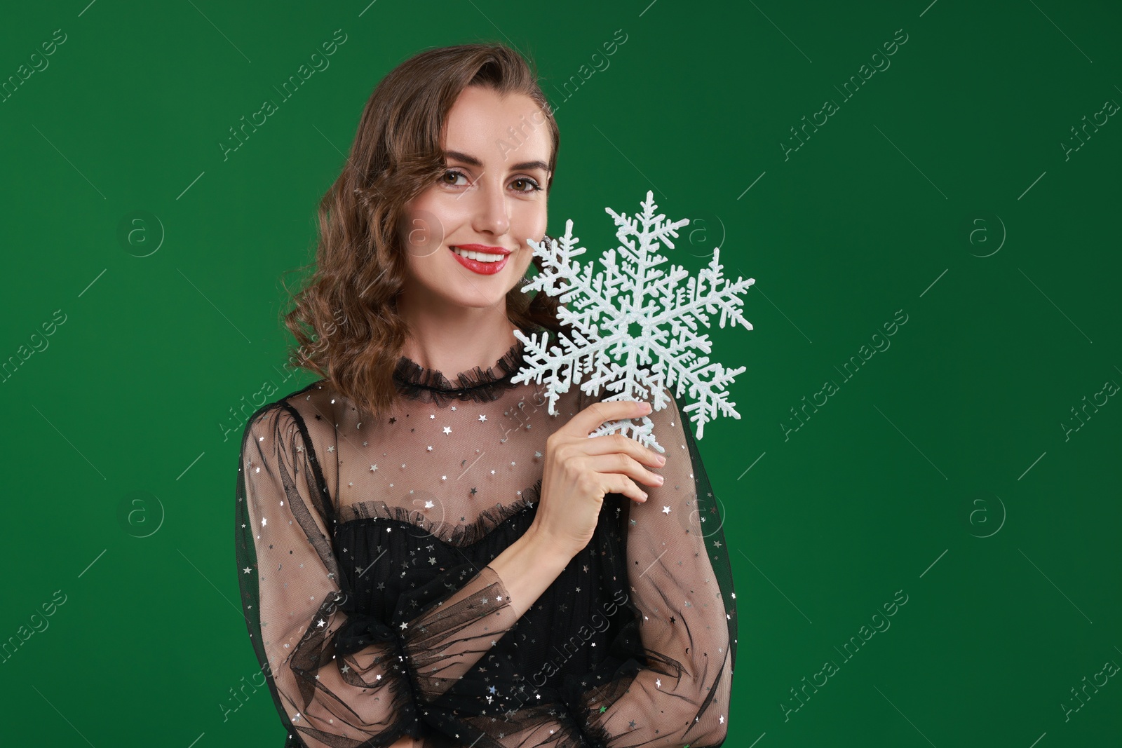 Photo of Smiling woman with perfect makeup holding decorative snowflake on green background. Christmas celebration