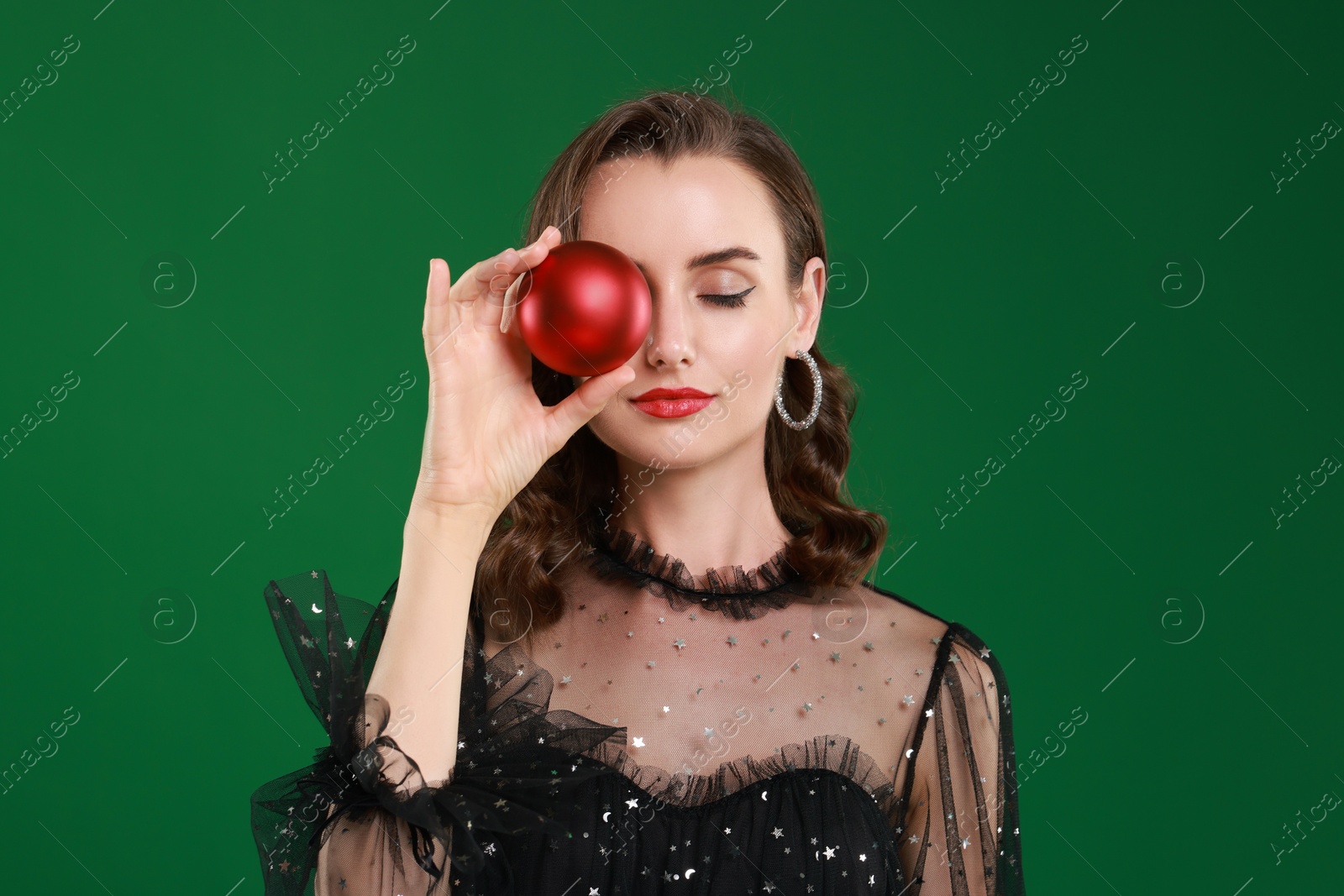 Photo of Woman with perfect makeup holding Christmas bauble on green background