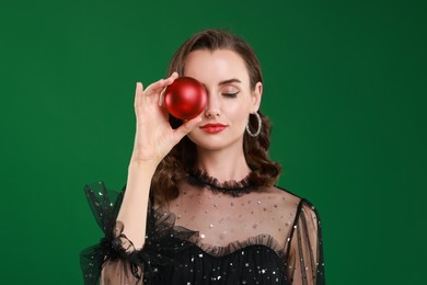 Photo of Woman with perfect makeup holding Christmas bauble on green background