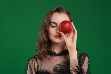 Woman with perfect makeup holding Christmas bauble on green background