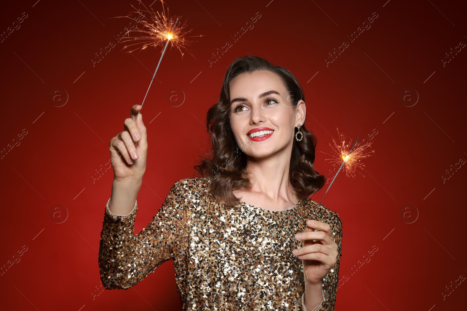 Photo of Smiling woman with sparklers celebrating Christmas on red background