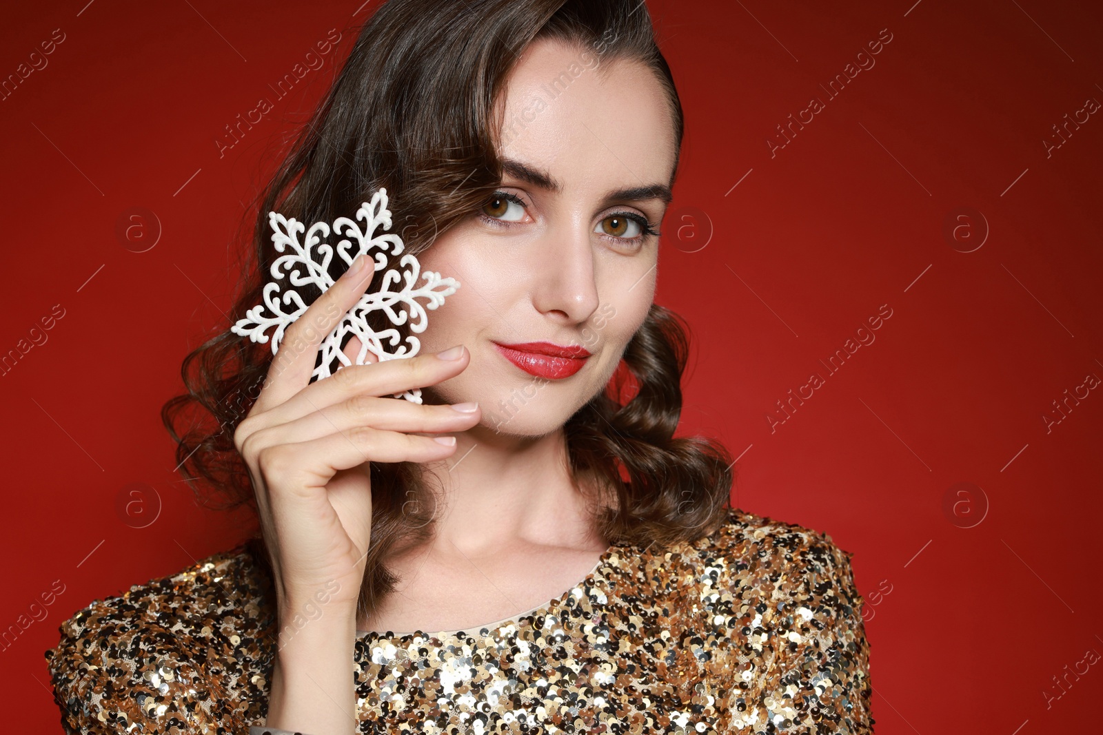 Photo of Woman with perfect makeup holding decorative snowflake on red background. Christmas celebration