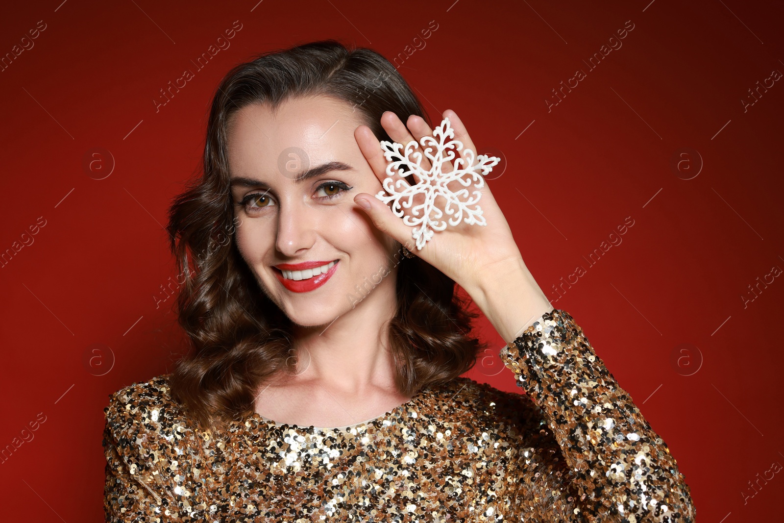 Photo of Smiling woman with perfect makeup holding decorative snowflake on red background. Christmas celebration