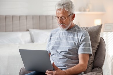 Photo of Senior man using laptop on armchair at home