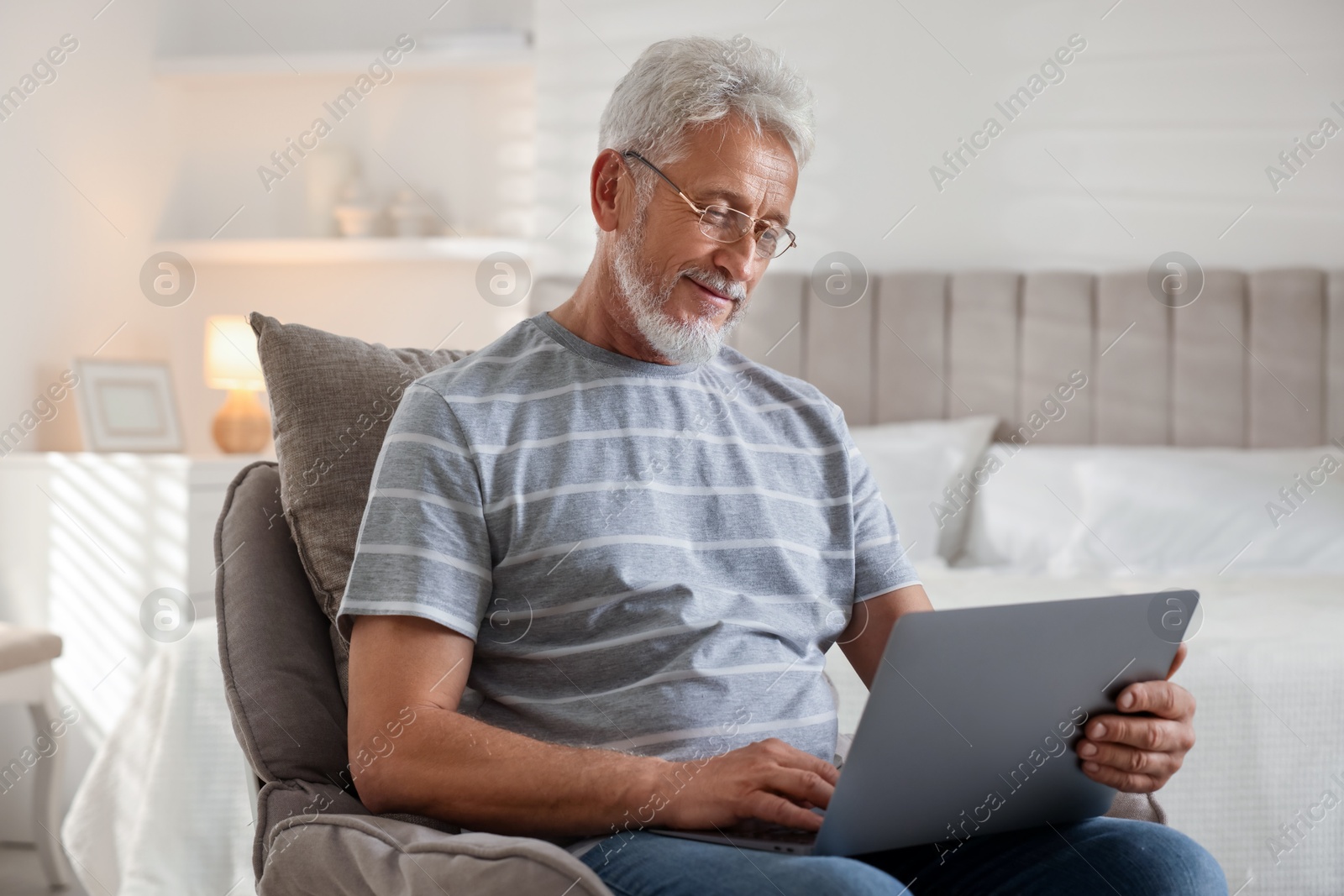 Photo of Senior man using laptop on armchair at home