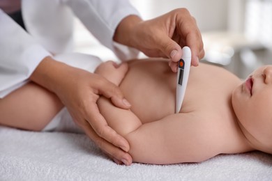 Photo of Pediatrician examining little child with thermometer in clinic, closeup. Checking baby's health