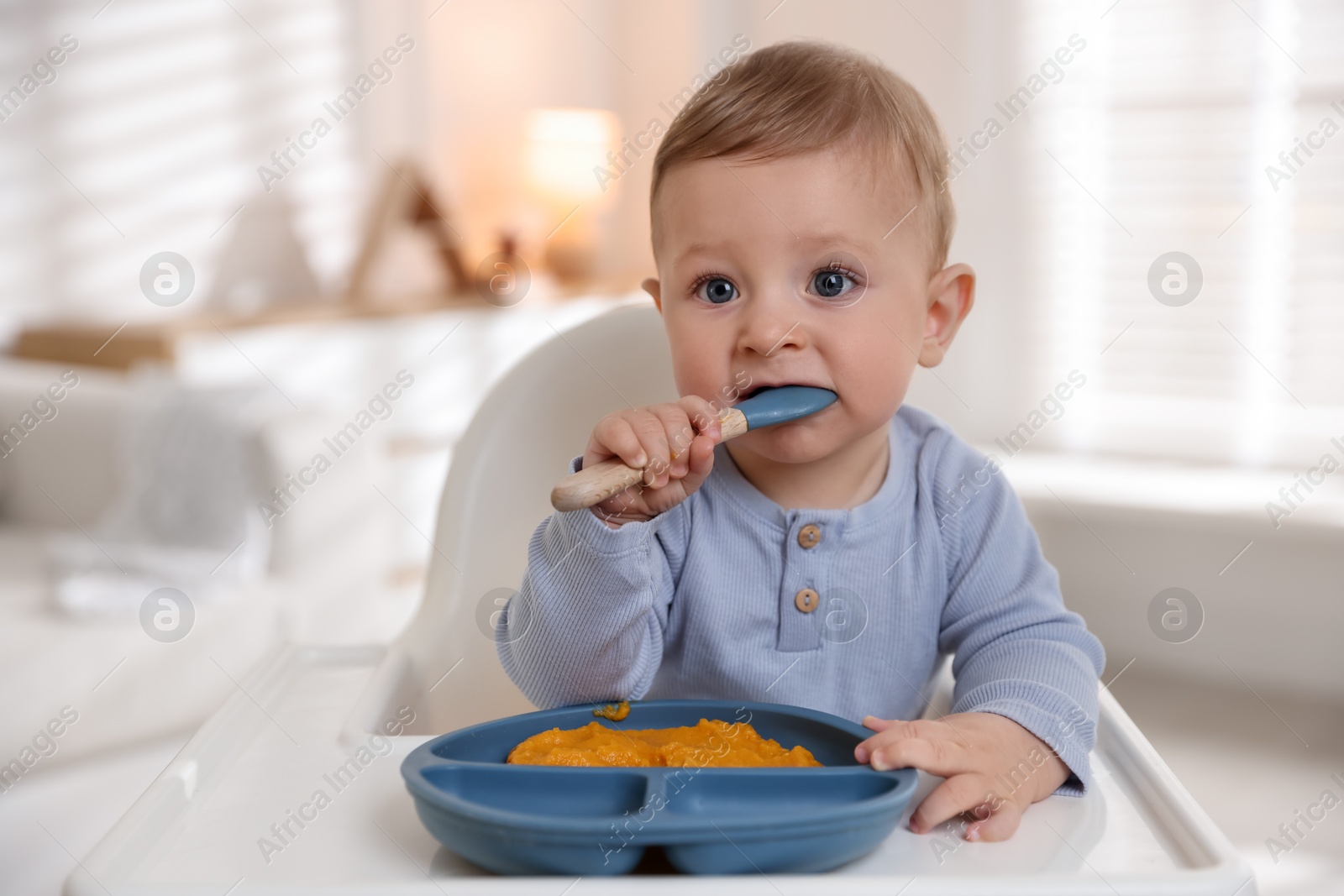 Photo of Cute little baby eating healthy food in high chair indoors