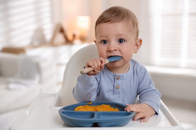 Photo of Cute little baby eating healthy food in high chair indoors