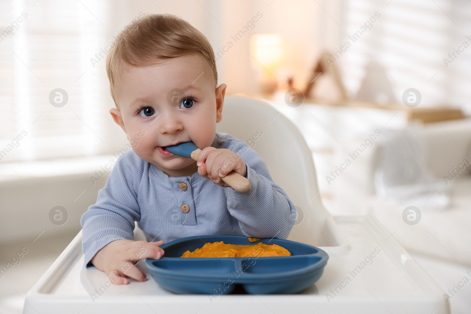 Photo of Cute little baby eating healthy food in high chair indoors