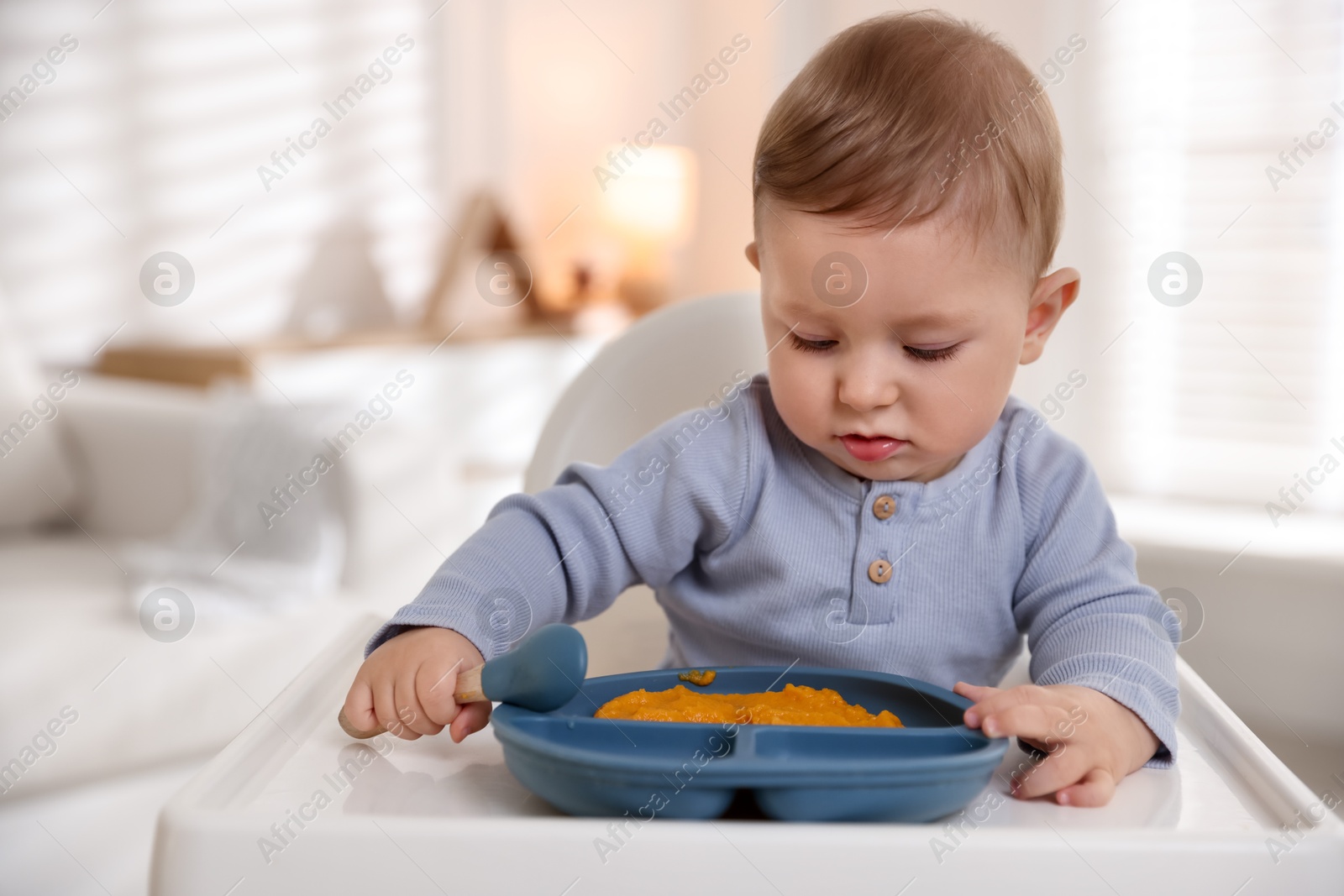 Photo of Cute little baby eating healthy food in high chair indoors