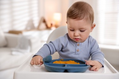 Photo of Cute little baby eating healthy food in high chair indoors