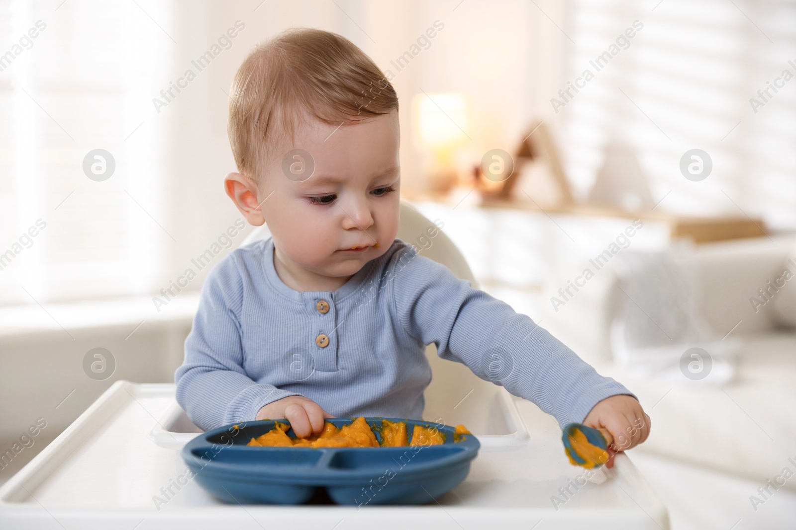 Photo of Cute little baby eating healthy food in high chair indoors